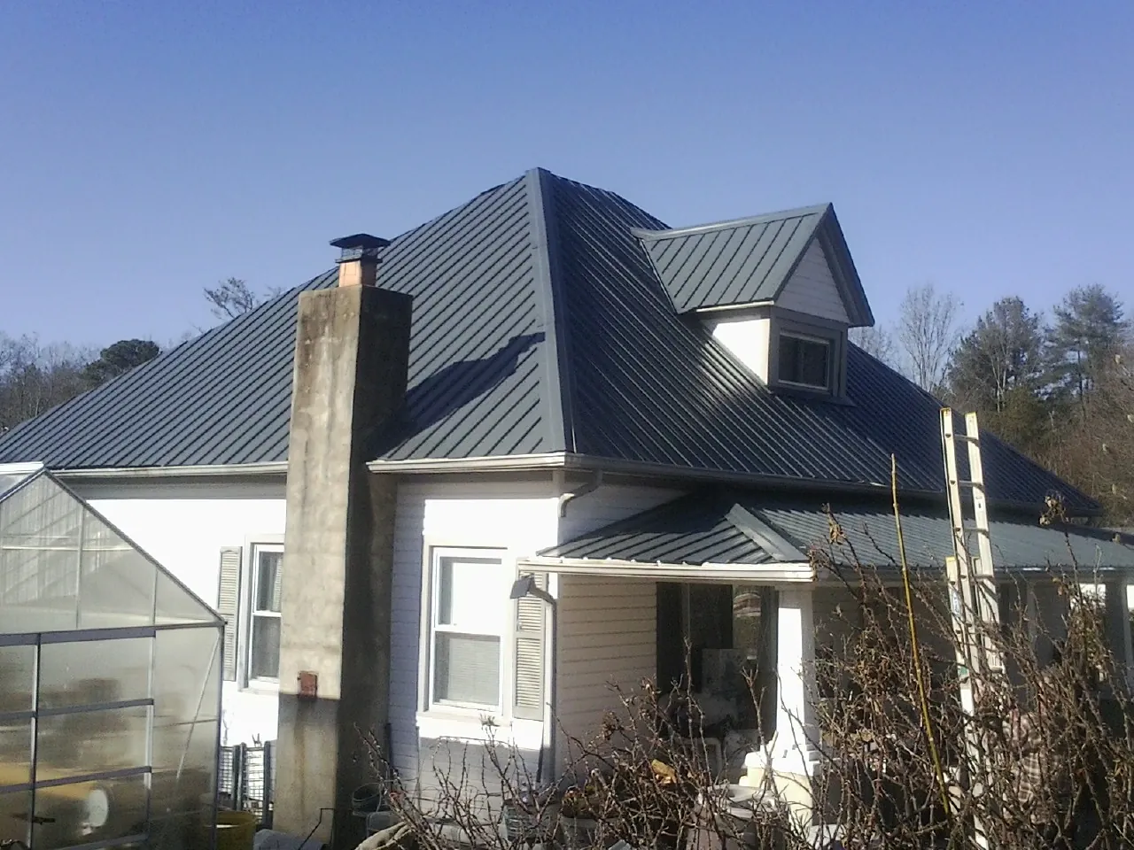 Dark blue standing seam metal roof on a white farmhouse with dormer — Slate & Tile Roof Repair by Roofing Brothers in Driftwood