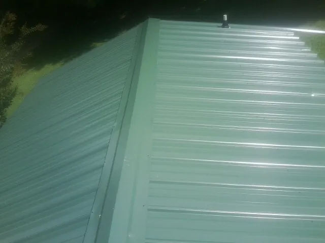 New green metal panels meeting at the ridge of a roof — Flat Roof Repair work by our crew in Driftwood
