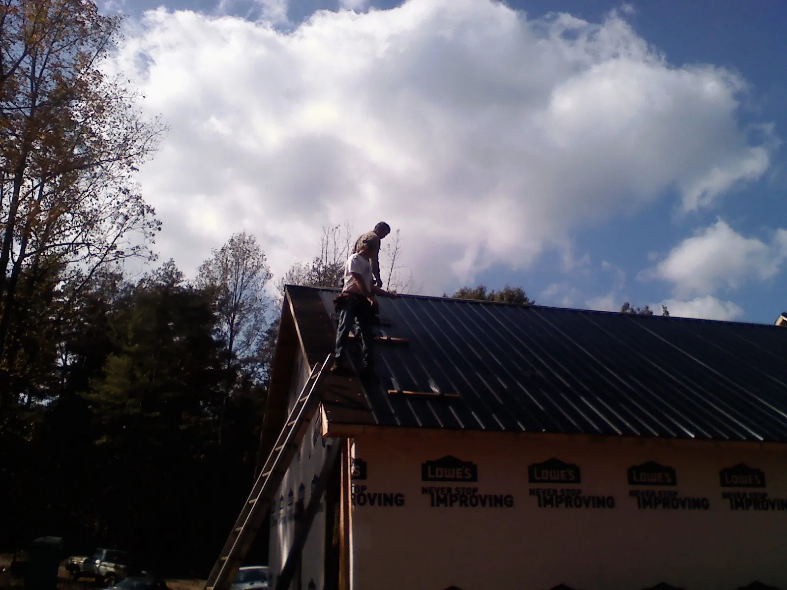 Roofer fastening dark metal panels high against a cloudy sky, from a Roof Inspection job in Driftwood