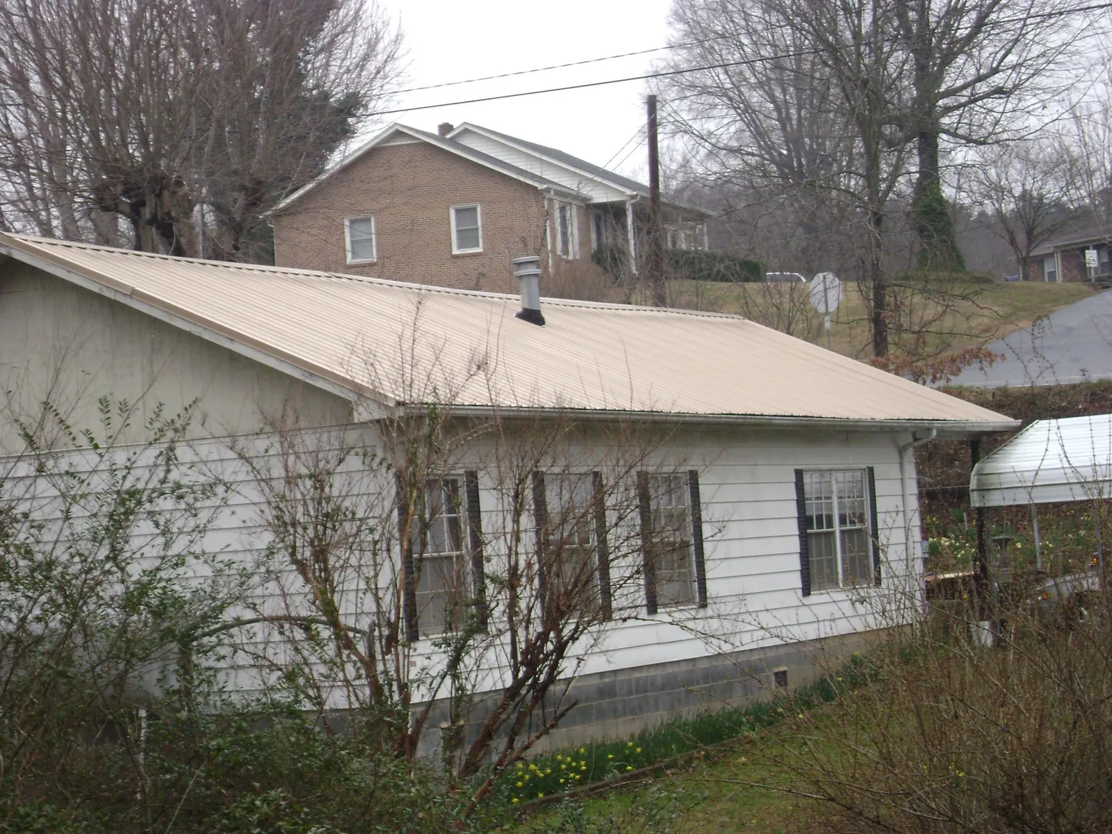 Tan metal roof on a white sided house set into a hillside — Commercial Roofing by Roofing Brothers in Driftwood