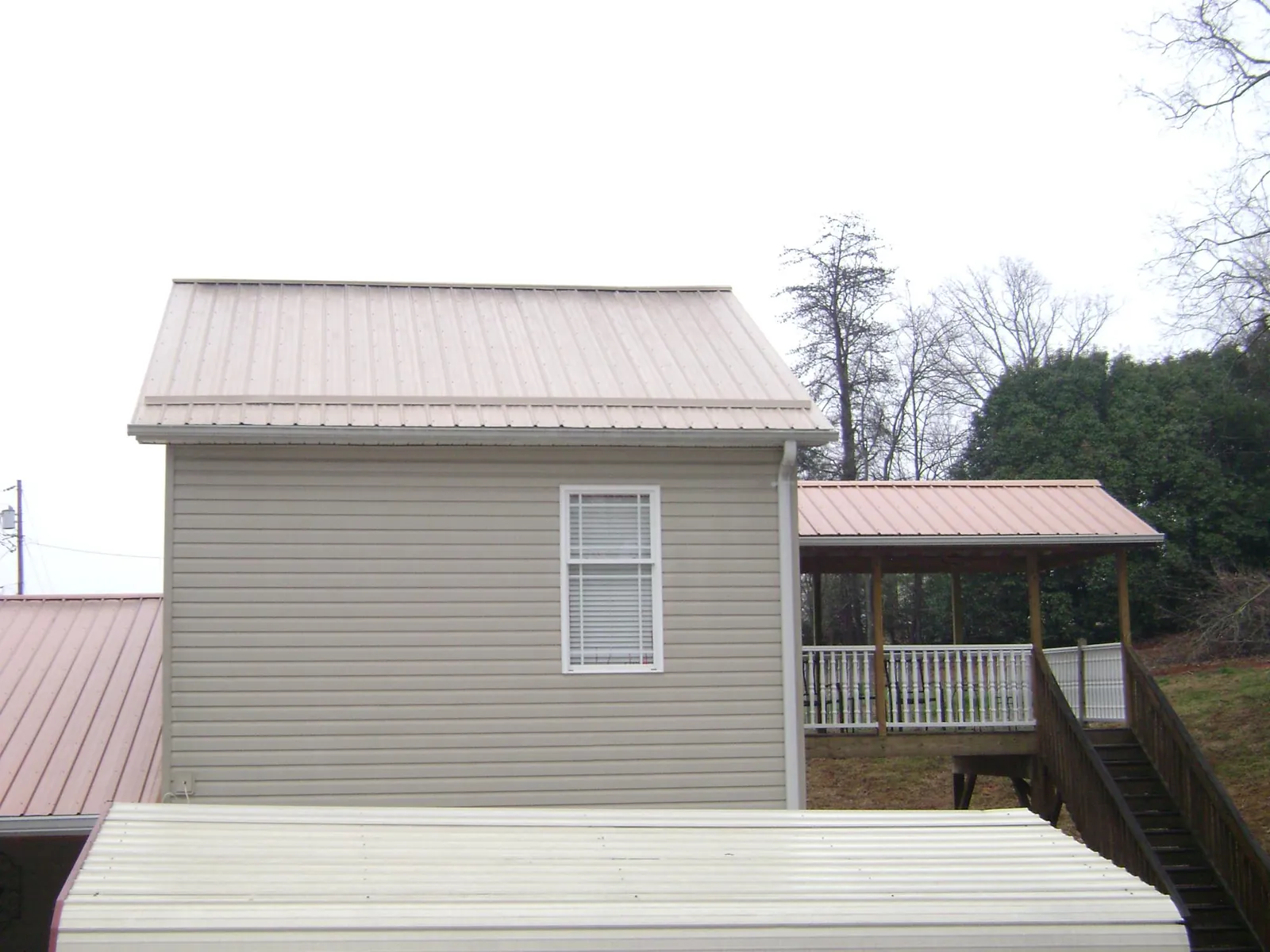 Tan metal roofs on a two story addition and attached porch, from a Roof Replacement job in Driftwood